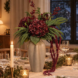 Julebuket i bordeaux og gran i en beige keramikvase midt på et dækket julebord med levende lys